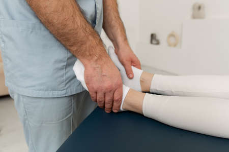 Knee pain relief in clinic. Doctor physiotherapist doing healing treatment on patient leg. Therapist giving leg and calf massage. Osteopathy, Chiropractic leg adjustment. Chiropractic treatment.の写真素材