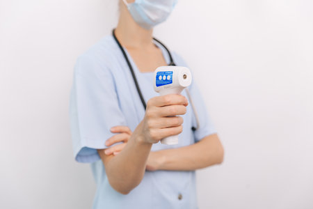 Temperature measurement gun in doctor hands. Close-up shot of doctor wearing protective surgical...