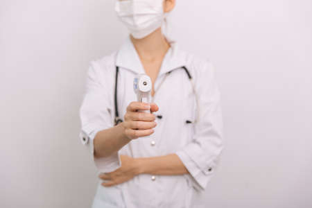 Temperature measurement gun in doctor hands. Close-up shot of doctor wearing protective surgical mask ready to use infrared isometric thermometer gun to check body temperature for virus symptoms.の写真素材