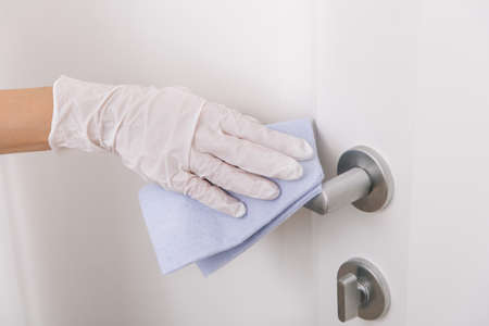 Cleaning door handle with blue wipe in white gloves.