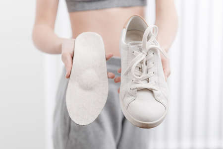 Woman putting orthopedic insole into shoe at home. Sports girl fitting orthopedic insole indoors,...