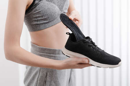 Woman putting orthopedic insole into shoe at home. Sports girl fitting orthopedic insole indoors,...