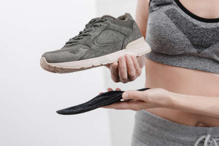 Woman putting orthopedic insole into shoe at home. Sports girl fitting orthopedic insole indoors,...