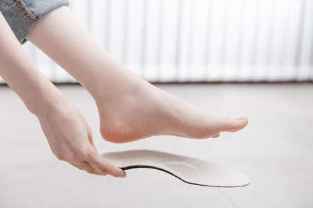 Woman fitting orthopedic insole indoors, close up. Girl holding an insole next to foot at home. Orthopedic insoles. Foot care banner. Flat Feet Correction. Treatment and prevention of foot diseases.の写真素材