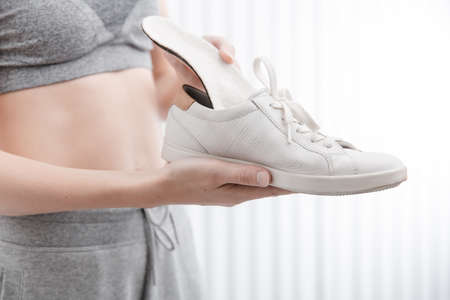 Woman putting orthopedic insole into shoe at home. Sports girl fitting orthopedic insole indoors, close up. Foot care banner. Flat Feet Correction. Treatment and prevention of foot diseases.の写真素材