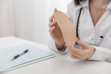 Doctor holding an insole while sitting at a table. Orthopedist tests the medical device. Orthopedic insoles. Foot care. Flat Feet Correction. Treatment and prevention of flat feet and foot diseases.の写真素材