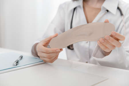 Doctor holding an insole while sitting at a table. Orthopedist tests the medical device. Orthopedic insoles. Foot care. Flat Feet Correction. Treatment and prevention of flat feet and foot diseases.の写真素材