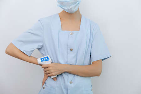 Temperature measurement gun in doctor hands. Close-up shot of doctor wearing protective surgical mask ready to use infrared isometric thermometer gun to check body temperature for virus symptoms.の写真素材