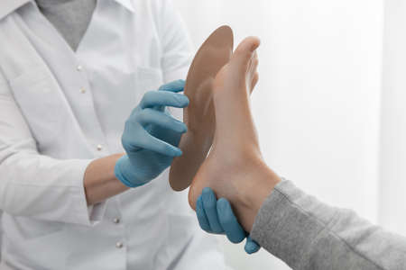 Doctor hands hold an orthopedic insole. Orthopedist tests the medical device. Orthopedic insoles on a white background. Foot care, comfort for the feet. Prevention of flat feet and foot diseases.の写真素材