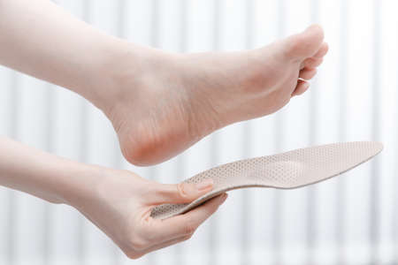 Woman fitting orthopedic insole indoors, close up. Girl holding an insole next to foot at home. Orthopedic insoles. Foot care banner. Flat Feet Correction. Treatment and prevention of foot diseases.の写真素材