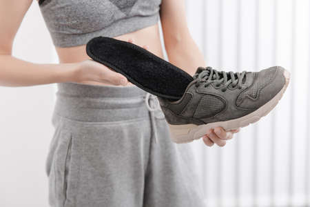 Fitness woman in sportswear with orthopedic insoles and sneakers. Woman putting orthopedic insole...