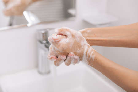 Washing hands under the flowing water tap. Hygiene concept hand detail. Washing hands rubbing with soap for corona virus prevention, hygiene to stop spreading corona virus in or public wash room.の写真素材