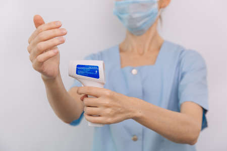 Temperature measurement gun in doctor hands. Close-up shot of doctor wearing protective surgical...