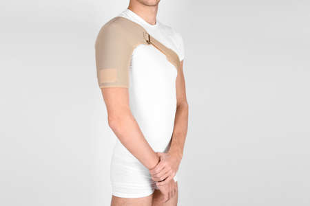 Shoulder joint orthosis or brace isolated on white background. A man in a support orthopedic bandage on his arms after surgery, suffering from shoulder pain, the result of a work injury.の写真素材