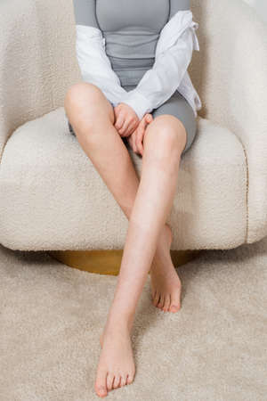 Long woman legs with smooth soft skin on sofa, couch or bed. A woman sits in a cozy home or apartment closeup. Woman doing skin care in the room. Beautiful sensual bare legs of a young woman.の写真素材