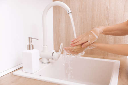 Washing hands under the flowing water tap. Hygiene concept hand detail. Washing hands rubbing with soapの写真素材