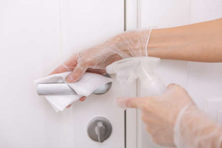 Cleaning door handles with wet wipe and white gloves. Sanitize surfaces prevention in hospital and...