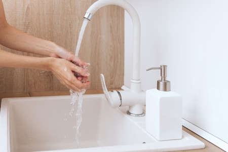 Washing hands under the flowing water tap. Hygiene concept hand detail. Washing hands rubbing with soap for corona virus prevention, hygiene to stop spreading corona virus in or public wash room.の写真素材