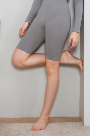 Long woman legs with smooth soft skin. A woman standing against the wall in a cozy home or apartment closeup. Woman doing skin care in the room. Beautiful sensual bare legs of a young woman.の写真素材