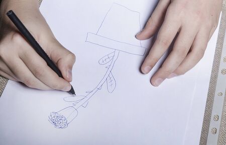 Hands of a child of European appearance. With one hand, the child draws with a ballpoint pen with a...