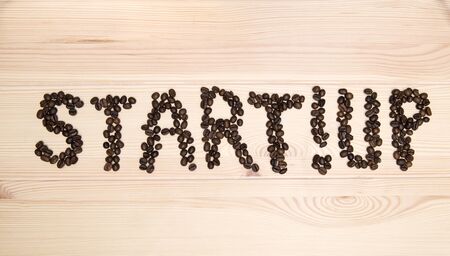 The word - start up - is made of roasted coffee beans on a light wooden textured surface of the table.の写真素材