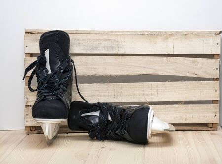 A pair of black hockey men's skates with sharp blades are located on a wooden tabletop made of light wood.の写真素材