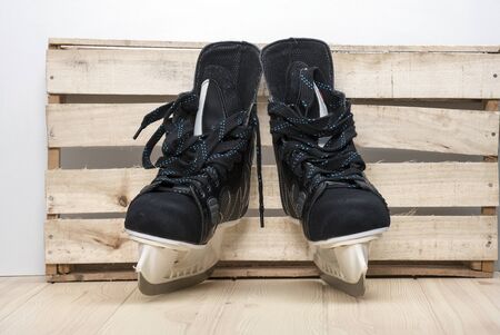 A pair of black hockey men's skates with sharp blades are located on a wooden tabletop made of light...