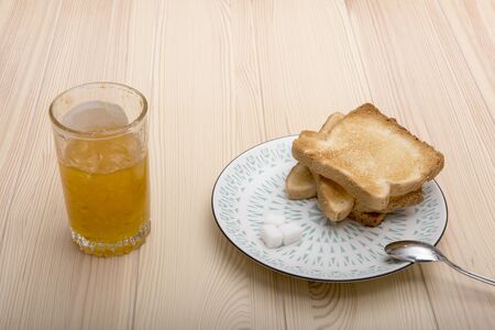 Breakfast. A glass with orange jam and a dish on which lie toasts, sugar and a teaspoon. Light wood table.の写真素材