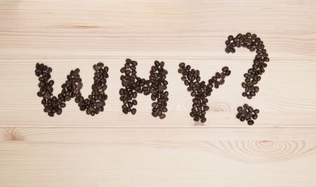 the word - why? The word - why and a question mark - are made of roasted coffee beans on a light wooden textured surface of the table.の写真素材
