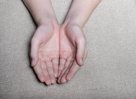 Hands of a child with white skin which he holds with palms up. Background - gray textured fabric
