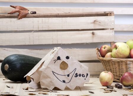 On a wooden textured light table lies a mask for the holiday of Halloween. Scattered around apples, zucchini, dry fallen autumn leaves, chestnutsの写真素材