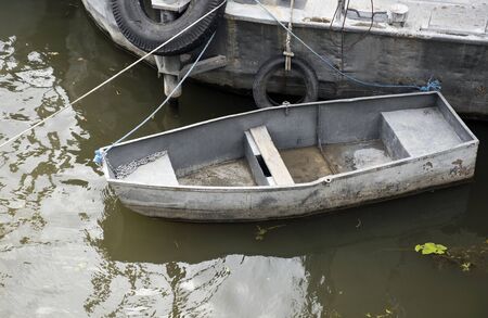 a boat. On the water, tied to a large vessel, an empty boat floats. The boat is old, with worn sides and a chain on the bow. Shabby tin on the sides of the boat. Algae swim in the muddy water on the water. Moscow, Russia, city center, Moscow river.の写真素材