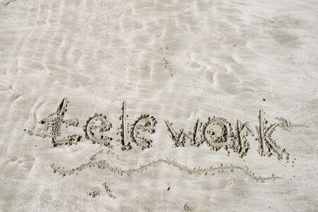 The beach, light dense sand on which the inscription is made in English: telework. Morning light of the bright sunの写真素材