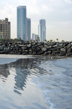 Ajman, United Arab Emirates. 01-27-2020. A large high-rise building of a delicate turquoise color is reflected on the wet sand of the sea beach. Small waves rush along the beachのeditorial素材