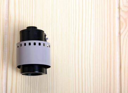 Photographic film in a black cassette lies on a light colored wooden table. Perforated film tail around containerの写真素材