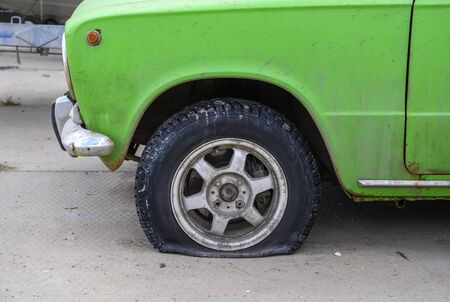 An old Soviet green Zhiguli car of emerald green color stands on the concrete floor of a garage with a flat tire waiting for repairs. Rusty car body with spots of dirt.の写真素材