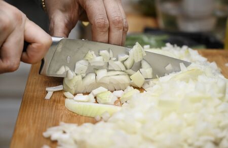 Female hands close-up. A woman holds a large sharp knife in her hand and cuts the onion into small...