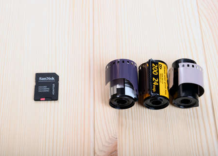One modern Sandisk micro SD memory card for a digital camera is on a wooden table opposite three old 35 mm films for the cameraのeditorial素材