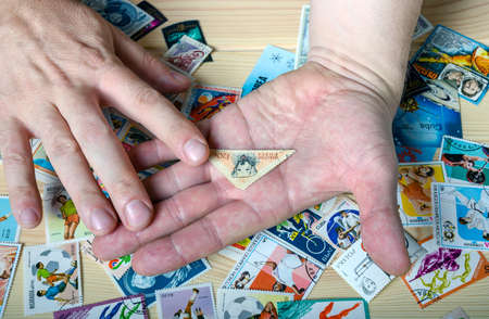 Dolgoprudny, Moscow region, Russia. 02-24-2020. Hands of a man holding a postage stamp with the stamp on which the dog is depicted. Stamps are scattered on the table.のeditorial素材