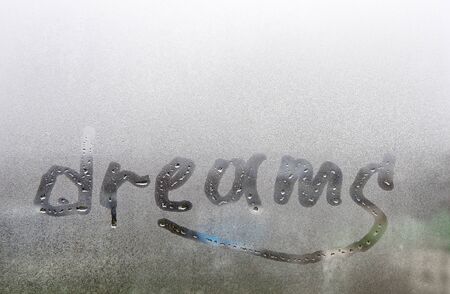 Dreams. The word - dreams - is written on wet, foggy glass. Traces of drops stretch from the letters