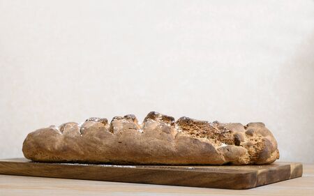 Side view of fresh gray hand made bread lies on a wooden board on a wooden fat table