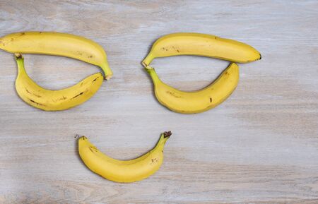 Yellow ripe bananas lie on a wooden vintage light surface of the table in the form of an image of a person's face with eyes and a smileの写真素材