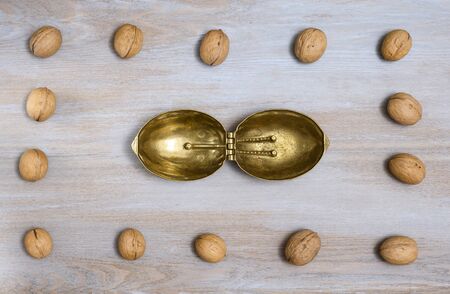 Walnuts are laid out on the edge of a wooden vintage light tabletop and in the center there is a horizontally open metal device for chopping nuts in the shape of a nutの写真素材
