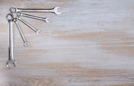Shiny metal keys are laid out in the upper left corner of a wooden vintage tabletop and form a...