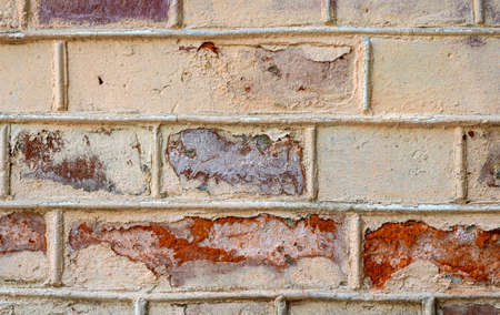 Textured ragged wall of red brick and yellow plaster. Fragment of the wall, street.