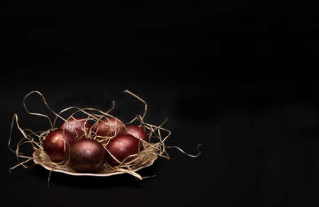Easter eggs with different textures in classic red on a saucer with straws on a black background....