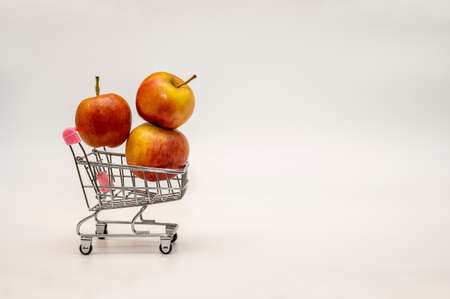 Small metal shopping trolley full of red ripe apples - isolate on a white background. Close-up, side view.の写真素材