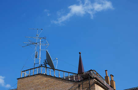 Satellite dishes and TV antennas on the roof of the house. Blue sky in sunny weather.