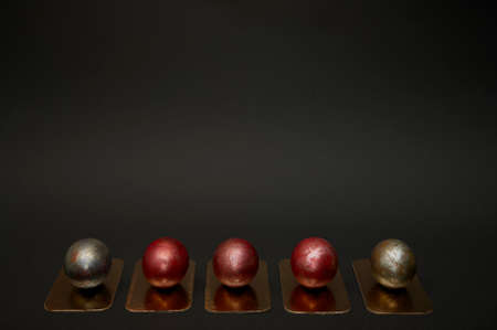 Five festive Easter eggs, painted in red and black paint, lie in one line on gold stands against a large black background - top view. Studio photography on a large banner.の写真素材