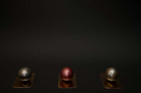 Three festive Easter eggs painted with red and black paint lie in one line on golden stands against...